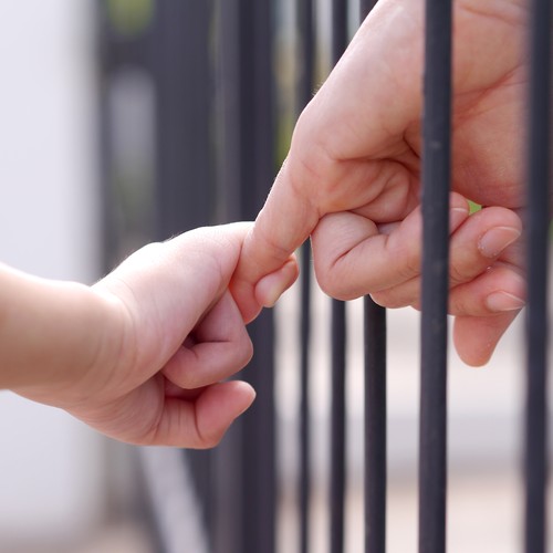 Zwei Hände halten sich durch Gitterstäbe